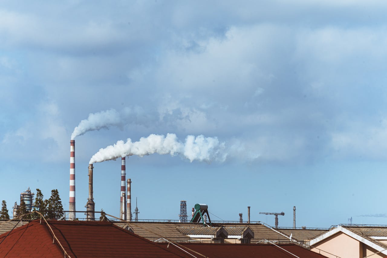 Factory chimneys emitting smoke over rooftops on a clear day, illustrating urban pollution.